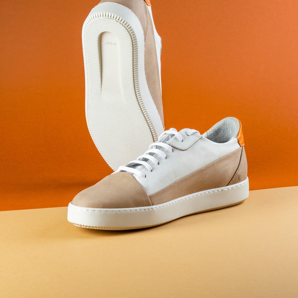 A pair of white and orange sneakers on an orange background.